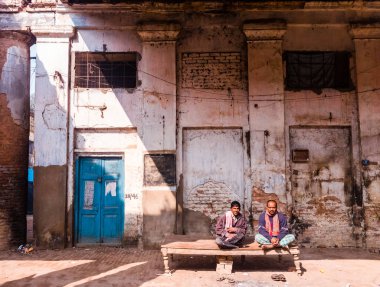 Murshidabad, Batı Bengal, Hindistan - Ocak 2018: Murshidabad 'da eski bir pazarın kirli binalarında ahşap bir bankta oturan iki adam.