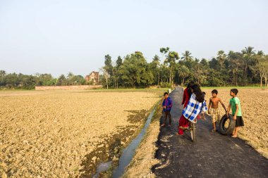 Murshidabad, Batı Bengal, Hindistan - Ocak 2018: Murshidabad kasabasındaki kırsal bir kırsal yolda bisiklet süren kızlar.
