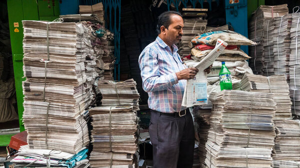 Калькутта, Западная Бенгалия, Индия - январь 2018: Индиец, читающий газету возле магазина бумаги на улицах города Калькутта.