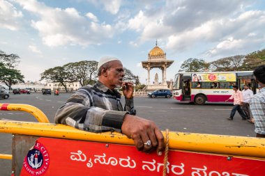 Mysuru, Karnataka, Hindistan - Ocak 2019: Mysore şehrinde yoğun bir trafik çemberinde yol kenarındaki bir bariyerin yanında duran Hintli Müslüman adam.