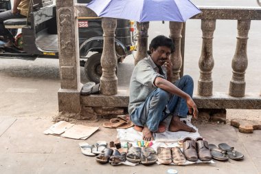 Mysuru, Karnataka, Hindistan - Ocak 2019: Mysore şehrinde kaldırımda şemsiye altında oturan bir sokak ayakkabıcısı.