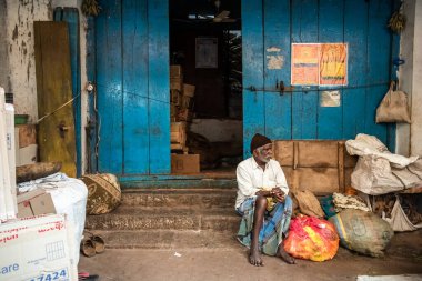 Mysore, Karnataka, Hindistan - Ocak 2019: Yaşlı Hintli bir adam, Mysuru kentindeki Devaraja Market 'in pis mavi ahşap kapılarının önünde oturuyor..