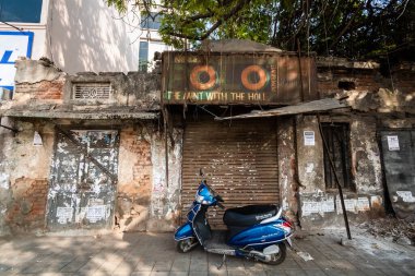 Bangalore, Karnataka, Hindistan - Ocak 2019: Kirli bir grungy dükkanının önüne park etmiş mavi bir scooter perdeler kapalıyken harap olmuş bir binada.
