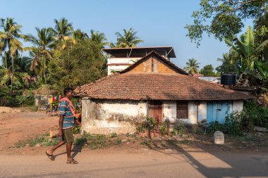 Mangalore, Hindistan - 18 Ocak 2023: Mangaluru yakınlarındaki bir köyde eski bir kır evinin önünden geçen Hintli bir adam.