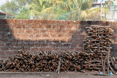 Mangalore, Hindistan - 18 Ocak 2023: Bir köyde taş bir duvarın dışına yığılmış büyük odun yığınları.
