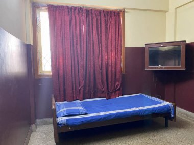 Mangalore, Hindistan - 17 Ocak 2023: Ucuz bir Hint otelinin basit bir odasındaki pencerenin altında tek bir karyola.