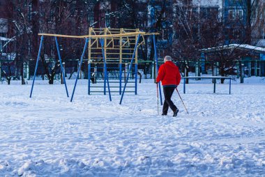 Yaşlı bir adam, kırmızı ceketli, kışın parkta yürüyen ya da kayak yapan bir İskandinav. Sağlıklı yaşam tarzı kavramı. Spor aktiviteleri