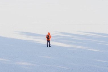 Turuncu ceketli bir adam donmuş bir gölde karda yürüyor.