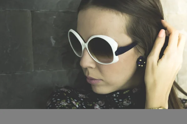 Young lady with sunglasses staying near brick wall — Stock Photo, Image