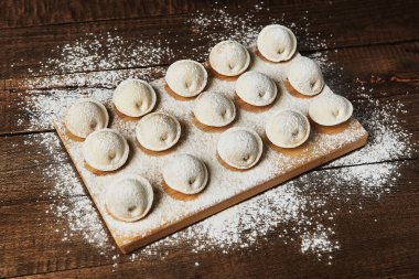 Ahşap arka planda çiğ hamur tatlısı üzerine un serpiştirilmiş.
