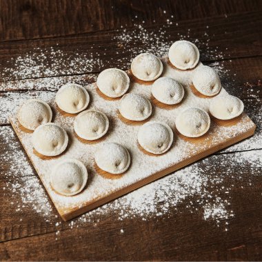 Ahşap arka planda çiğ hamur tatlısı üzerine un serpiştirilmiş.