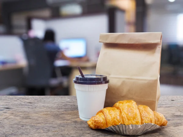 Kávét és croissant-t a papírzacskót, a fából készült asztal — Stock Fotó