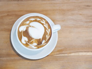 Tahta masanın üzerinde sütlü sütlü latte ile kaplanmış bir fincan kahve. Görünümün üstünde