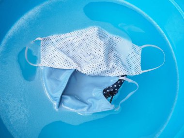 Kirli yüz maskesini mavi havuzda yıkamak için deterjan köpüğüne batırmanın üst görüntüsü.