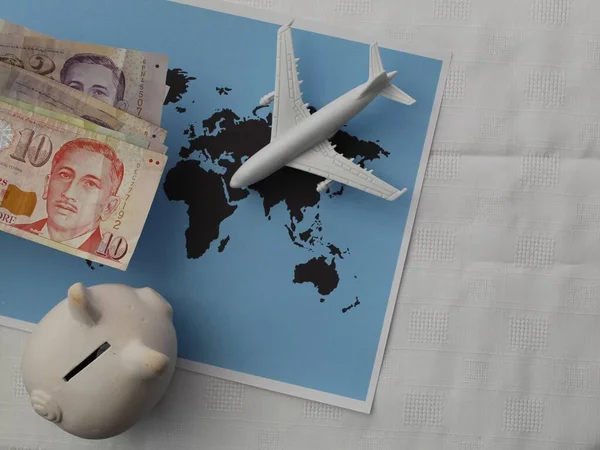 singaporean money, piggy bank and plastic airplane figure on a world map