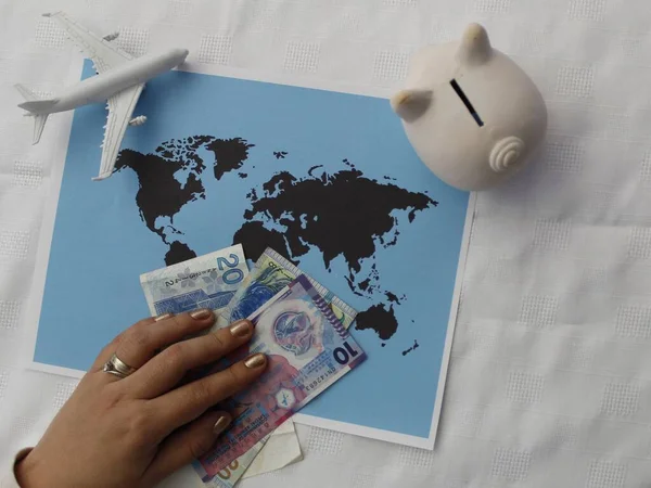 hand holding Hong Kong money, piggy bank and plastic airplane figure on a world map