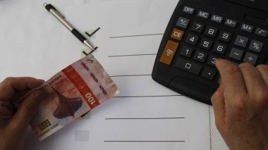 Masada Norveç banknotu, hesap makinesi, kalem ve hedef listesi tutan eller