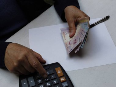 Brezilya banknotları ve hesap makinesi tutan bir kadının elleri.