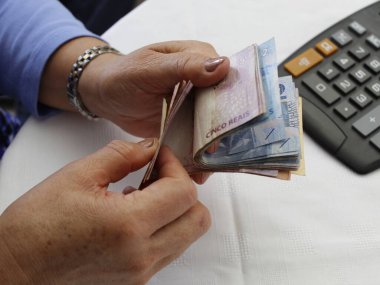 Masadaki Brezilya banknotlarını ve hesap makinesini sayan bir kadının elleri