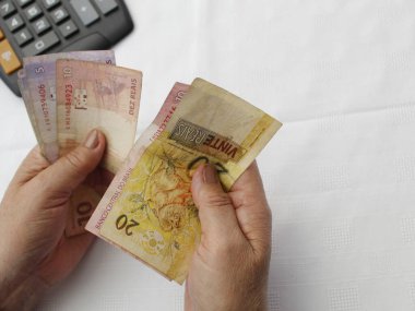 Masadaki Brezilya banknotlarını ve hesap makinesini sayan bir kadının elleri