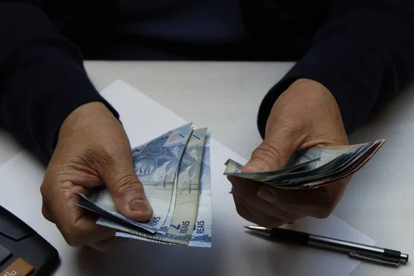Brezilya banknotlarını ve kalemleri sayan bir kadının elleri.