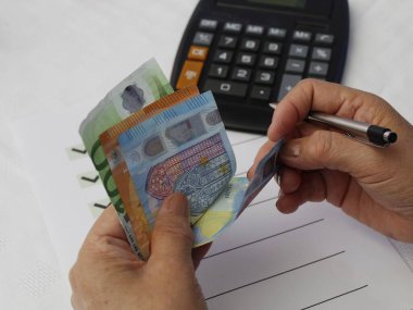 Avrupai banknotları sayan, hedefler listesi ve masada hesap makinesi olan bir kadının elleri