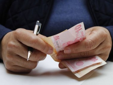 Elinde Türk banknotları ve kalemle yaşlı bir kadının ellerine yaklaş.