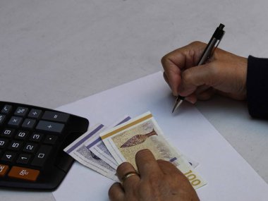 Elinde Danimarka banknotları ve hesap makinesi olan bir kalem tutan yaşlı bir kadının elleri.