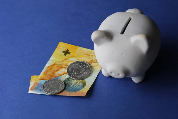 swiss banknote, coins and white piggy bank on the blue background