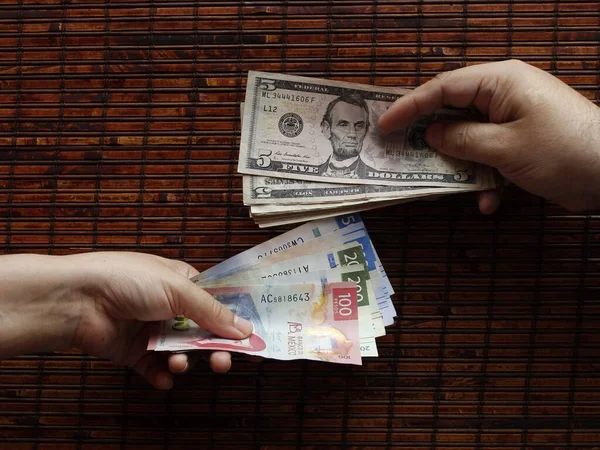 Amerikan banknotları ve Meksika banknotları değiş tokuş eden iki kişinin elleri.