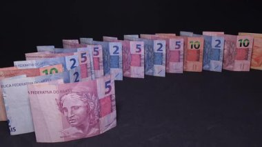 Brazilian real banknotes falling in a slow-motion domino effect on a black background