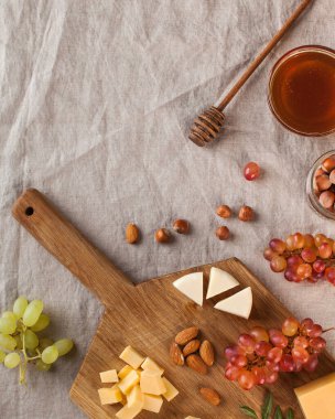 Peynir tabağı. Tahta bir tahtanın üzerinde üzümlü peynirler, tatlım, keten bir masa örtüsünün üzerinde fındıklar. Yüksek kalite fotoğraf
