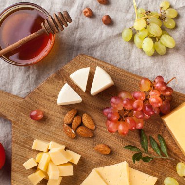 Peynir tabağı. Tahta bir tahtanın üzerinde üzümlü peynirler, tatlım, keten bir masa örtüsünün üzerinde fındıklar. Yüksek kalite fotoğraf