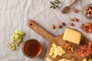 Peynir tabağı. Tahta bir tahtanın üzerinde üzümlü peynirler, tatlım, keten bir masa örtüsünün üzerinde fındıklar. Yüksek kalite fotoğraf