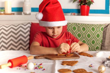 Noel Baba şapkalı şirin çocuk zencefilli ekmeği dikkatlice süslüyor. Yüksek kalite fotoğraf