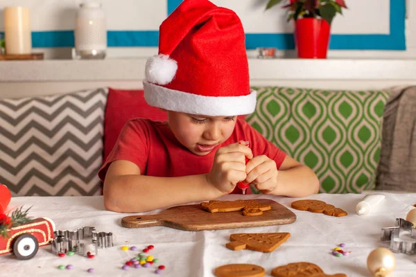 Noel Baba şapkalı şirin çocuk zencefilli ekmeği dikkatlice süslüyor. Yüksek kalite fotoğraf