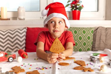 Noel Baba şapkalı bir çocuk Noel ağacı şeklinde zencefilli kurabiye tutuyor. Yeni yılın zencefilli çöreğini pişiriyorum. Yüksek kalite fotoğraf