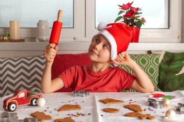 Noel Baba şapkalı şirin bir çocuk masada zencefilli ekmek yapar ve elinde kırmızı bir oklavayla gezer. Yüksek kalite fotoğraf