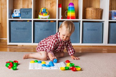 Bir çocuk, çocuk odasındaki halının üzerinde plastik bir mozaikle oynuyor. Erken gelişim, Montessori yöntemi..
