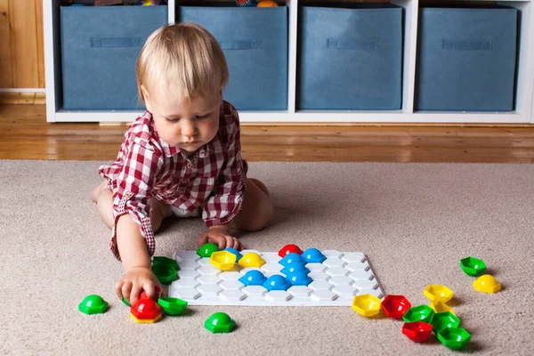 Un niño pequeño juega con un mosaico de plástico en la alfombra de la habitación de los niños. Desarrollo temprano, el método Montessori. —  Fotos de Stock