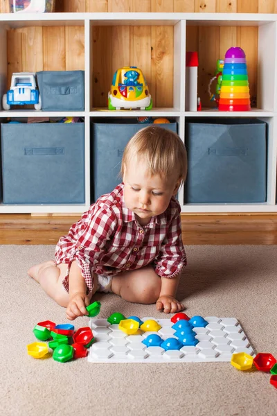 Un niño pequeño juega con un mosaico de plástico en la alfombra de la habitación de los niños. Desarrollo temprano, el método Montessori. —  Fotos de Stock