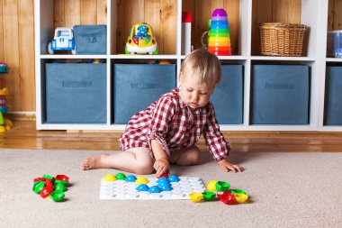 Bir çocuk, çocuk odasındaki halının üzerinde plastik bir mozaikle oynuyor. Erken gelişim, Montessori yöntemi..