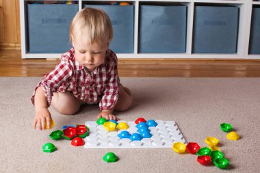 Bir çocuk, çocuk odasındaki halının üzerinde plastik bir mozaikle oynuyor. Erken gelişim, Montessori yöntemi..