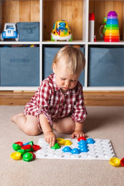 Bir çocuk, çocuk odasındaki halının üzerinde plastik bir mozaikle oynuyor. Erken gelişim, Montessori yöntemi..