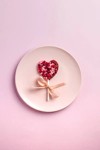 Chocolate heart on a pink plate on a pink background. The concept of a romantic dinner, Valentines Day. Copy space. — Stock Photo, Image