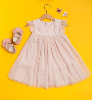 Childrens festive outfit on a yellow background. Cute baby pink dress with shoes and hairpins.
