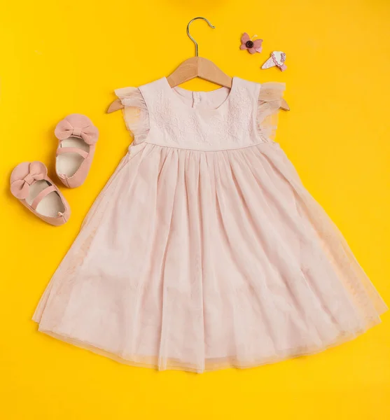 Childrens festive outfit on a yellow background. Cute baby pink dress with shoes and hairpins.