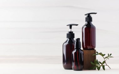 Tahta blokta yeşil yapraklı doğal organik kozmetik ürünleri olan üç farklı kahverengi şişe. Boşluğu kopyala 