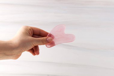 Bir kadın elinde guaj taşı masaj kazıyıcısı tutuyor. Moda güzellik tedavileri. Boşluğu kopyala.