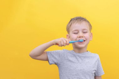 Tatlı sarışın çocuk dişlerini fırçalıyor ve sarı arka planda gülümsüyor. Boşluğu kopyala.